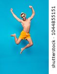 Small photo of Fullbody, full length portrait of attractive, successful, cheerful, foolish, comic ladies' man in yellow shorts, jumping with open mouth and raised hands, isolated on blue background
