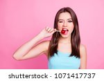 Portrait of lovely sweet cute charming beautiful cheerful hungry adorable gorgeous woman with straight brown hair trying to bite red lollipop  on stick, isolated on bright pink background