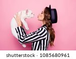 Side view, half face, profile portrait of attractive, pretty, charming girl raise dog in front of face, blowing kiss to pet, isolated on pink background