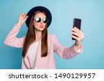 Small photo of Portrait of dreamy cute girl using her mobile phone making selfie sending air kisses launching blog stream wearing pink stylish topcoat isolated over blue background