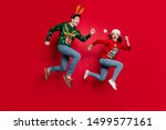 Full body photo of amazed jumping couple excited by x-mas prices hurry shopping wear ugly ornament jumpers isolated red color background