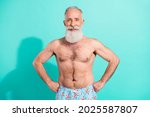 Portrait of attractive cheerful grey-haired bearded man swimmer hands on hips isolated over bright teal turquoise color background