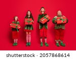Full length body size view of attractive cheerful company elf holding dream boxes isolated over bright red color background