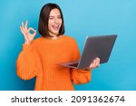 Portrait of attractive cheerful skilled girl using laptop showing ok-sign winking isolated over bright blue color background