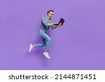 Small photo of Photo of excited bust guy wear grey shirt spectacles jumping high typing modern device isolated violet color background