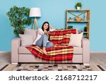 Portrait of attractive cheerful girl sitting on divan staying alone watching film relax isolated on blue color background indoors