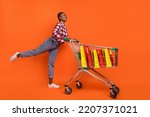 Full length photo of excited positive girl push cart look empty space isolated on orange color background