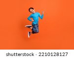 Small photo of Full size photo of charming small pupil boy jump play raise fists celebrate dressed stylish blue look isolated on orange color background