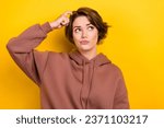 Small photo of Portrait of ponder pensive girl bob hair dressed brown sportswear scratches her head look empty space isolated on yellow color background