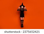 Full length photo of funny excited girl dressed dark witch dress headwear jumping high isolated orange color background