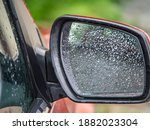 Closeup of car side rear view mirror with rain drops