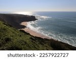 A small beach with a rocky sea coast wall with a beautiful contrast between the sea with waves and a coastal plain of stones and a blue sky