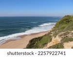 A small beach with a rocky sea coast wall with a beautiful contrast between the sea with waves and a coastal plain of stones and a blue sky