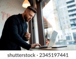 Man working on his laptop while enjoying a cup of coffee. A man holding a coffee cup and looking at a laptop