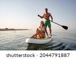 Couple of tourists young man and woman having fun paddleboarding at sea