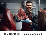 Young Butcher Holding Raw Meat...