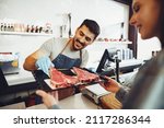 Small photo of Butcher's shop seller helps to choose product to woman customer