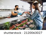 Small photo of Butcher's shop seller helps to choose product to woman customer