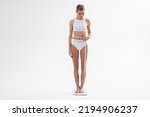 Small photo of Daily morning measurement. Dieting results. Slim woman in underwear measuring body during losing weight marathon standing on weight scales and checking waist line with tape measure, isolated on white
