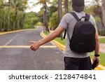 Adult man backpacker in cap standing by the road with thumb up, tourist hitchhiking, hailing taxi, traveling.