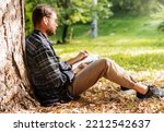 Adult man writings in his diary while sitting on the ground in nature.
