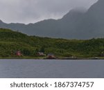 Idyllic view of traditional wooden rorbu houses with red painted facade located on the shore of Raftsundet on Hinnøya island, Vesterålen, Norway with rugged mountains in background on cloudy day.