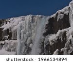 Beautiful view of the top of Öxarárfoss waterfall in rocky Almannagjá canyon in Þingvellir national park, part of Golden Circle, Iceland, in winter season with snow and icicles on sunny day.