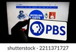Small photo of Stuttgart, Germany - 10-01-2022: Person holding cellphone with logo of American tv network Public Broadcasting Service (PBS) on screen in front of webpage. Focus on phone display. Unmodified photo.