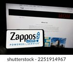 Small photo of Stuttgart, Germany - 01-13-2023: Person holding smartphone with logo of US online shop company Zappos.com LLC on screen in front of website. Focus on phone display. Unmodified photo.