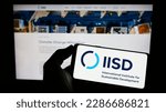 Small photo of Stuttgart, Germany - 04-01-2023: Person holding mobilephone with logo of think tank IISD institute on screen in front of web page. Focus on phone display. Unmodified photo.