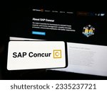 Small photo of Stuttgart, Germany - 07-11-2023: Person holding smartphone with logo of expense management software SAP Concur on screen in front of website. Focus on phone display. Unmodified photo.