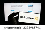 Small photo of Stuttgart, Germany - 07-11-2023: Person holding mobile phone with logo of expense management software SAP Concur on screen in front of business web page. Focus on phone display. Unmodified photo.