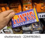 Small photo of Dortmund, Germany - Feb 19, 2022: POV male hand holding package pack with Tony's Chocolonely toffee chocolate with shelves in supermarket in background