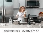 Small photo of Child washing dishes near sink in kitchen. Child with sponge with dish washing liquid is doing the dishes at home kitchen by using wash sponge and dish washing.