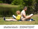Small photo of Father read a book with son in a park outdoors. Father and child son reading outdoor on green nature background. Dad with kid reading book together in the summer park. Family reading a book in nature.