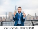 Small photo of Winner Dollars. Businessman with dollars money. Excited man with dollar money on street. Rich business man in suit hold dollar cash. Businessman hold 100 dollars banknotes at city. Dollars banknote.
