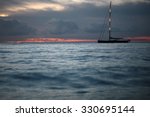 Small photo of Beautiful calm evening seascape with silhouette of yacht under bare poles floating in blue sea waves after red sunset in background on the horizon distant view, horizontal picture