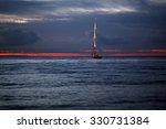 Small photo of Beautiful calm evening seascape with yacht sailing in dark blue seaways under bare poles floating in the sea in rays of amazing red sunset on horizon against red and blue cloudy sky, horizontal photo