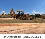Small photo of KB, Malaysia - 1 Oct 21: Backhoe is leveling a crusher run at construction site. A backhoe is a type of excavating equipment, consisting of a digging bucket on the end of a two-part articulated arm.