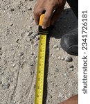 Small photo of A man is using a measuring tape to take measurements on the ground. A tape measure or measuring tape is a flexible ruler used to measure length or distance.