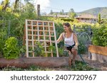 Small photo of A young woman waters her garden. A cedar trellis can be a beautiful additional and also provide important support to climbing and vining plants, taking advantage of vertical space