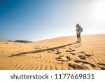 Small photo of single man explorer in the desert with jacquet equiment and backpack traveling and walking barefoot. discover the beauty of the world in alternative vacation and lifestyle. wanderlust concept