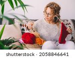 Adult attractive woman at home in knitting work activity using colorful wool. Happy and relaxed female people enjoying time indoor on the sofa. Knit job