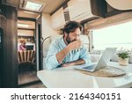 Couple use computer inside camper van during travel vacation or van life lifestyle. Modern man and woman work together on laptop in alternative office motor home. Digital nomad and smart free working