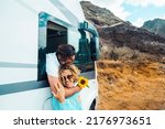 Happy traveler couple enjoy summer destination with camper van. Van life and off grid alternative house style. Man hug woman from inside a modern camper van. Love and travel two people lifestyle