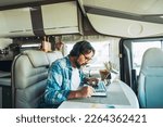 One handsome mid age man working on mobile cell phone and laptop computer inside a camper van sitting at the table. Modern online business job and traveler people lifestyle. Transport and vehicle