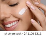 Woman with beautiful face touching healthy facial skin portrait. Beauty close up girl is applying a skincare product. Hydration. Cream smear. 
