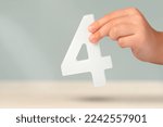 Small photo of number four in hand. Hand holding white number 4 on blurred background with copy space. Concept with number four. Birthday 4 years, fourth grade, four day work week