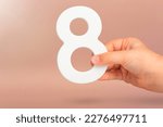 Small photo of Eight in hand. A hand holds a white number 8 on a red background. Concept with number eight. Birthday 8 years, percentage, eighth grade or day, international women's day.