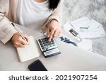 woman writing a list of debt on notebook calculating her expenses with calculator with many invoices , female hand doing accounting 